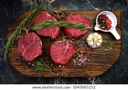 fresh raw fillet minion steaks marbled beef with rosemary and garlic on wooden background, top view