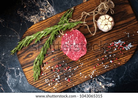 fresh raw fillet minion steak marbled beef with rosemary and garlic on wooden background
