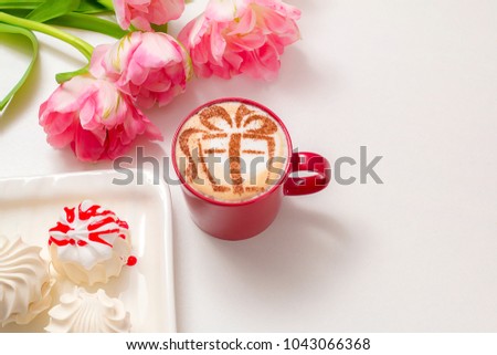cappuccino in a red mug with a picture of a gift on milk foam surrounded by flowers of tulips and sweet marshmallows