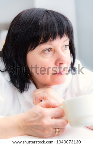 brunette middle-aged woman in the morning in bed with a cup of coffee