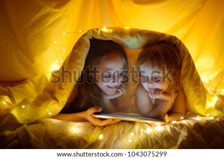 Two kids using tablet pc under blanket at night.  Royalty-Free Stock Photo #1043075299