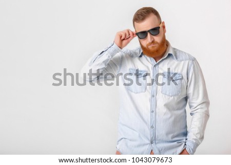smiling red-haired beard man in sunglasses and denim shirt on gray background. copy space