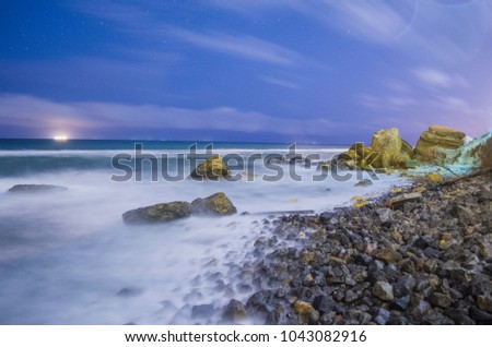 Night landscape of the sea. the beach is strewn with stones, and waves on long exposure are washed by rocks sticking out of the water. The clouds fly away.