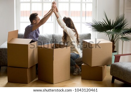 Excited couple holding hands happy to move into new home, young family celebrate moving day sitting on sofa with boxes, tenants renters or owners relocating into house start living together concept Royalty-Free Stock Photo #1043120461