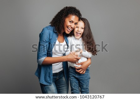 Love you so much. Nice mother embracing her little daughter while standing together isolated on grey background