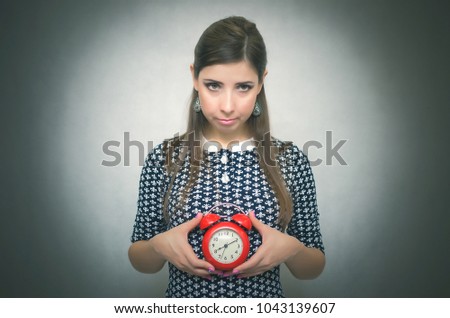 Guilty look woman holding in hands alarm clock and hides her eyes by looking aside. Latecomer student or emloyee. Be late at work or school. Oversleep concept.