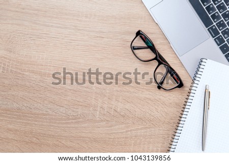Flat lay photo of wooden office desk with laptop, eyeglasses, pen and notebook with copy space background.