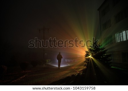 Night Landscape. City at night in dense fog. Mystical landscape surreal lights with creepy man. The walking man's silhouette in night fog at artificial light. Beautiful mixed lighting from backside.