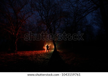 strange light in a dark forest at night. Silhouette of person standing in the dark forest with light. Dark night in forest at fog time. Surreal night forest scene. Horror halloween concept. Fairytale
