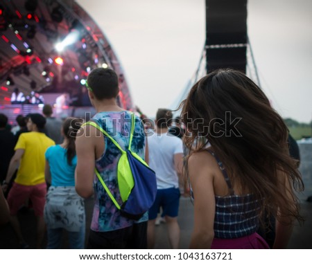 Back view of group of dancing people on the dance floor at music festival. Young trendy persons has fun outdoors