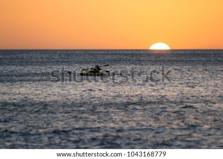 Young man kayaking in the ocean as the sun goes down for the evening