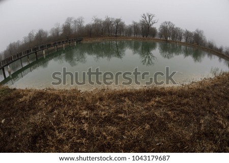 Forest lake with bridge during the sunny day with winter trees and blue cloudy sky. Beautiful natural mountain lake with forest in the background and stormy clouds on the sky. Azerbaijan nature