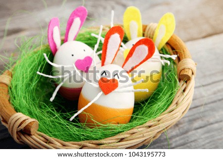 Eggs with funny rabbit faces in basket on grey wooden table