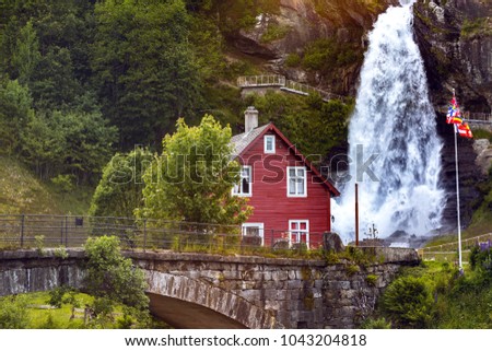 traditional norwegian red wooden house and steinsdalsfossen waterfall in the background, norway
