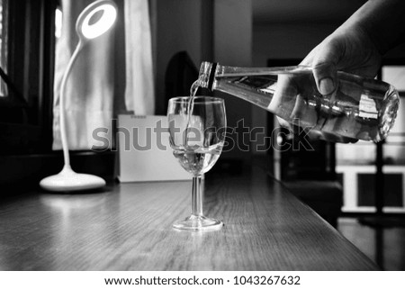 Pouring the drinking water into glass of wine on working table. Black and white picture tone