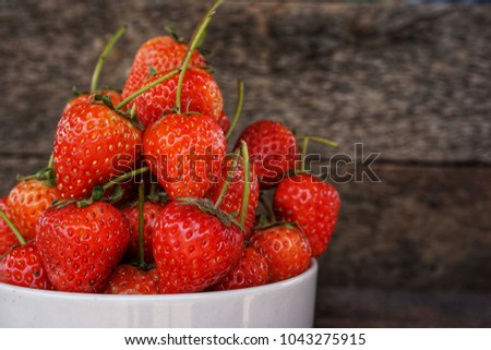 Strawberries in the white ceramic Bowl placed on the old wooden floor.