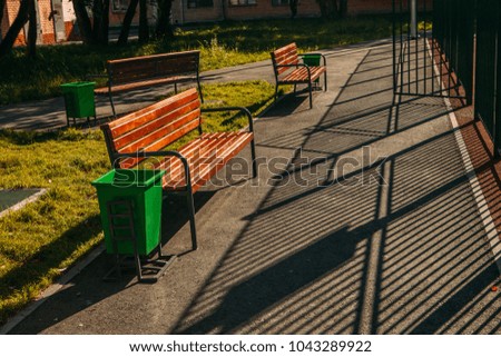 bench with trashcan in park summer outdoor with shadows of fence