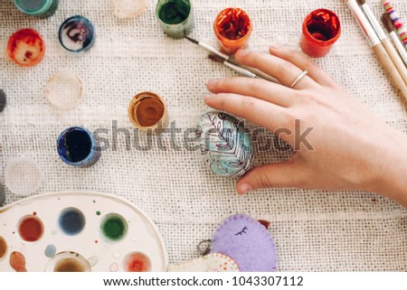 hand holding colored easter egg on rustic background with colorful paint. kids playing and coloring eggs, easter hunt concept. flat lay