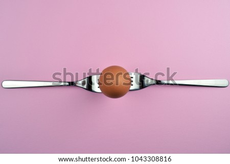 Egg on the white, purple, blue, pink background in center. Design, visual art, minimalism. Conceptual image balanced on forks