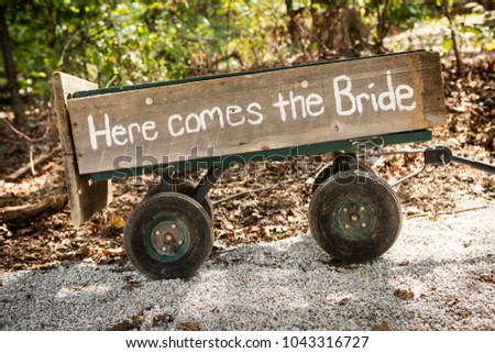 Small wooden hindcarriage with white hand painted Here comes the Bride sign on board. Funny wedding decoration idea