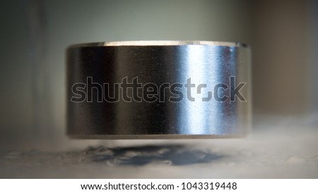 levitating neodymium magnet. A levitating magnet over a superconductor filled with liquid nitrogen Royalty-Free Stock Photo #1043319448