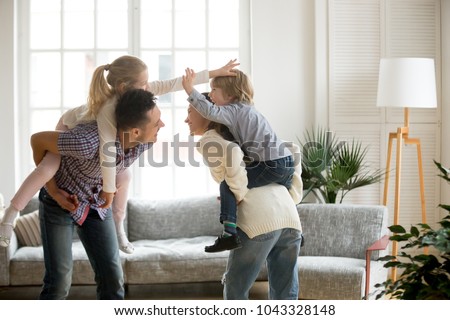 Happy young parents piggybacking son and daughter at home, smiling father and mother holding little kids on back spending time together, family having fun enjoying activity playing with children Royalty-Free Stock Photo #1043328148