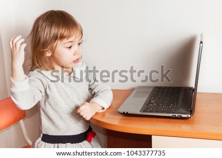 Litttle baby girl sitting at the laptop on light  background.
