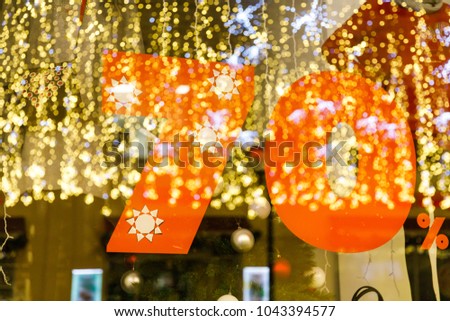 Large Sale 70 percent discount, a banner on the glass with the reflection of New Year's garlands.
