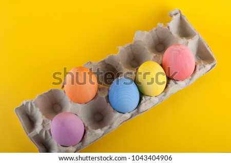Top view on colored Easter eggs laying in paper container on yellow background
