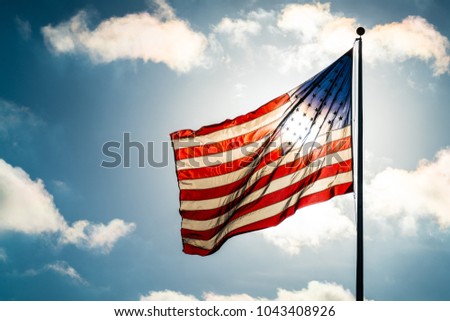 Close up on Stars and Stripes waving in the breeze the national American flag illuminated back lit by sun. United States flag waving in the wind on a dramatic sky day