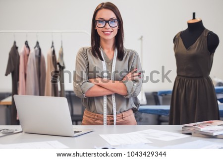 Attractive fashion designer is looking at camera and smiling while standing with crossed arms in her office