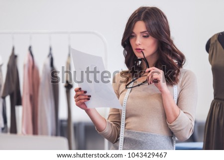 Beautiful fashion designer is holding eyeglasses and studying a sketch while working in her office