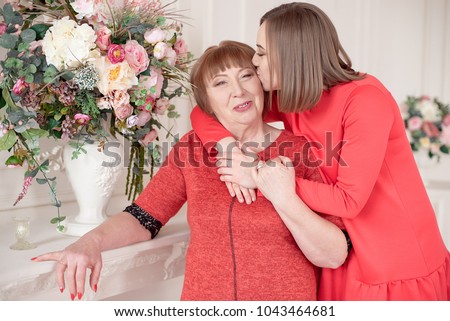 Daughter hugs and kiss Mature Mother standing behind her.