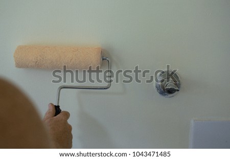 A man holding the rolling paint to paint the wall with the old water tap