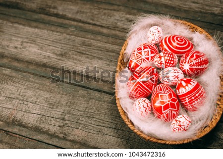 Red easter eggs with folk pattern lay on white feather in the basket which stand on vintage wooden board. Ukrainian traditional eggs pisanka and krashanka