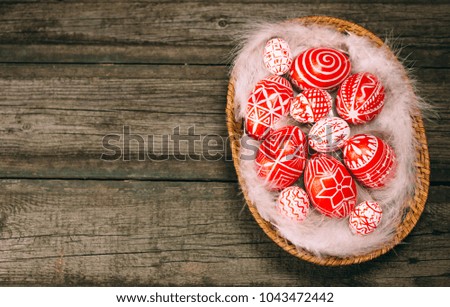 Red easter eggs with folk Ukrainian pattern lay on white feather in the basket which stand on vintage wooden board.