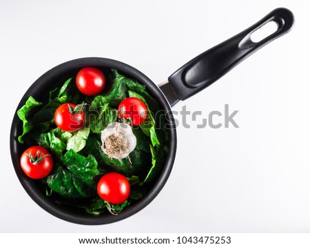 Stock pot with fresh green spinach, cherry tomatoes and garlic.