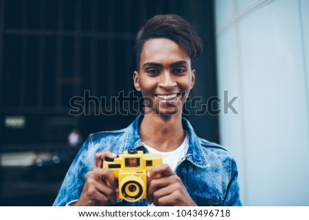 Half length portrait of successful skilled photographer with beautiful smile holding modern yellow camera in hands to making cool photos standing outdoors on urman promotional background