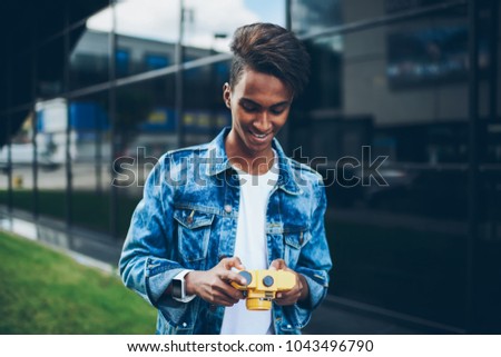 Positive male hindu photographer looking funny pictures on digital photo camera and laughing while watching standing outdoors.Cheerful skilled amateur making setting for taking photos