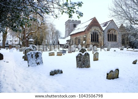  snow scene of Ringmer Church, East sussex, UK, the church and the grave yard in the foreground, a weeping willow tree to the left and the church on the right all covered in a thick layer of snow. 