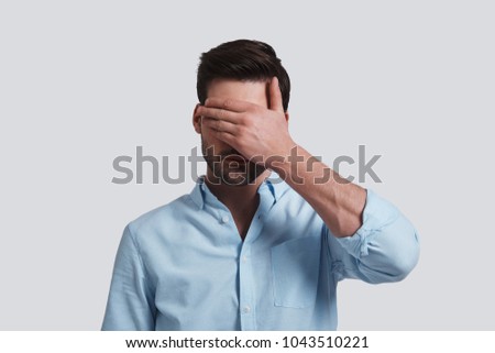 See nothing.  Handsome young man covering eyes with hands while standing grey background Royalty-Free Stock Photo #1043510221