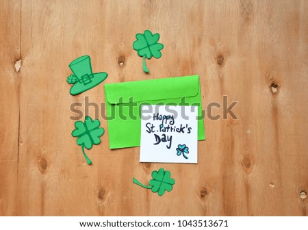 Paper Green Clovers or Shamrocks and an envelope with Happy St. Patrick's Day text on a note on rustic wooden table