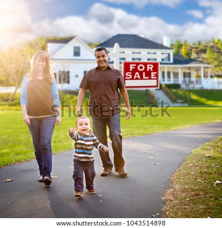 Happy Mixed Race Family Walking in Front of Home and For Sale Real Estate Sign.