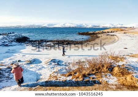 Adorable little girl and cute boy enjoying snowy winter day outdoors at beach surrounded by fjords in Northern Norway