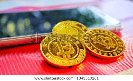 Selective focus of Bitcoin gold coin and blurry smartphone on red table background. Virtual cryptocurrency concept  