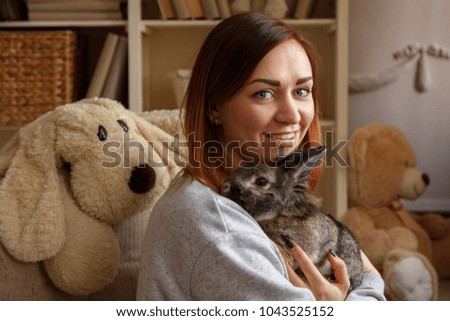 Happy woman holding Easter bunny and smiling to camera at home at Easter day