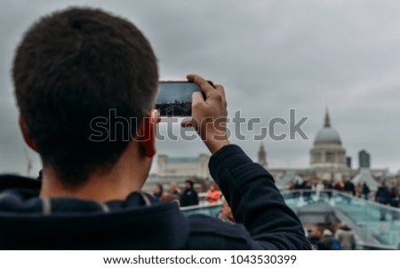 Young man taking a picture using his smartphone of the Millenium Bridge and St. Paul's Cathedral in London, England, UK.