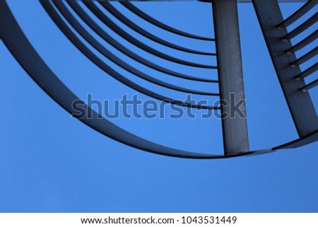 Close up view from bellow of iron decorative curved elements. Blue sky in background. Circular lines silhouettes. Geometric abstract image. Pattern of grey metallic arcs and semi circles. Urban image.