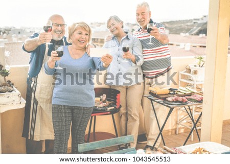 Happy seniors friends taking a selfie photo with smartphone at barbecue dinner in patio house - Mature people having fun and drinking wine - Focus on left couple - Joyful elderly lifestyle concept