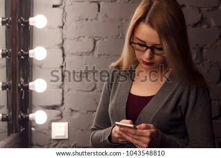 Attractive female in elegant dress reading news in network on cell telephone while is sitting in modern cafe,confident businesswoman using her smart phone while relaxing after work day in coffee shop